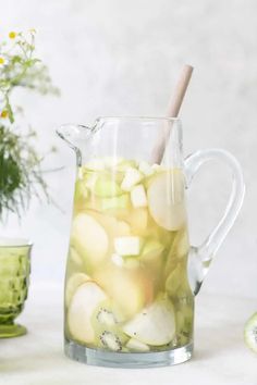 a pitcher filled with water and sliced fruit on top of a table next to flowers