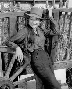 black and white photograph of woman in cowboy hat leaning on an old wagon with hay behind her