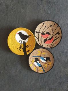 three woven coasters with birds on them sitting next to each other in front of a gray background