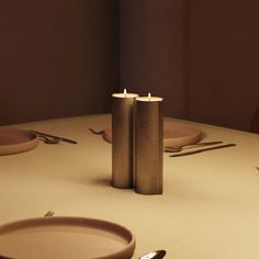 two candles sitting on top of a table next to plates and silverware with utensils