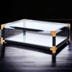 a glass and wood coffee table on a hard wood floor with black walls in the background