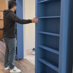 a man standing in front of a blue book shelf with shelves on each side and one hand reaching for something