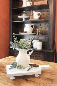 a wooden table topped with a white vase filled with flowers and greenery on top of it