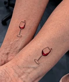 two people wearing matching tattoos with wine glasses on their arms and feet, one holding a glass of red wine