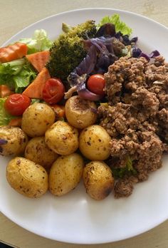 a white plate topped with potatoes and meat next to broccoli, lettuce and tomatoes