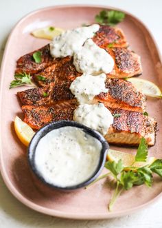 grilled salmon with tartar sauce and lemon wedges on a pink platter