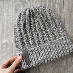 a hand is holding onto a gray knitted beanie on a wooden surface,