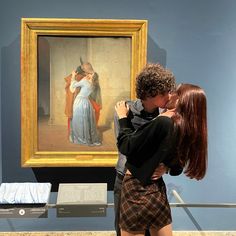 a man and woman kissing in front of a painting