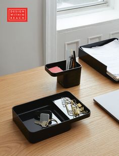 a wooden desk topped with two black trays filled with office supplies