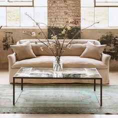 a living room with a couch, coffee table and vase on the floor in front of large windows