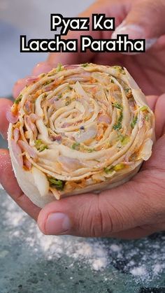 a person holding food in their hand with the words pyaz ka laccha paratha