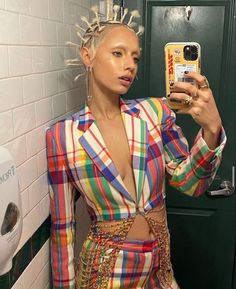 a woman taking a selfie with her phone in a bathroom stall wearing a multicolored suit