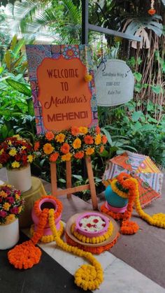 a welcome sign with flowers and decorations on the ground in front of some plants,