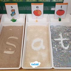 three trays filled with sand and letters on top of a wooden table next to each other