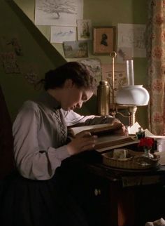 a man sitting at a desk with some books in front of him and a lamp on top of the table