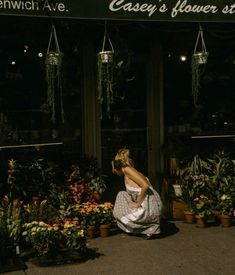 a woman kneeling down in front of a flower shop