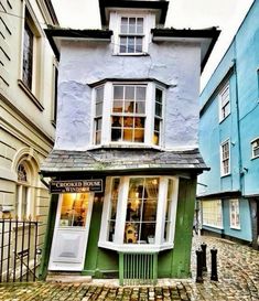 a small green building sitting on the side of a cobblestone road next to tall buildings