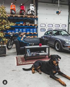 a man sitting on a couch next to a black and brown dog in a garage