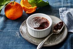 a bowl of powdered sugar sits on a plate next to an orange and spoon