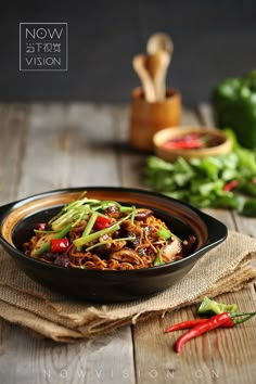 a bowl filled with meat and vegetables on top of a wooden table next to green peppers