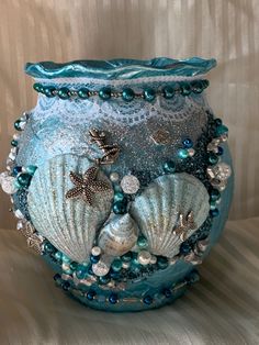 a blue vase with sea shells and pearls on the bottom is sitting on a table