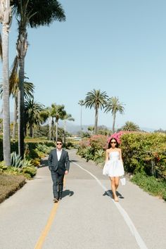 a man and woman walking down a road with palm trees in the backgroud