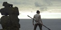 a woman standing on top of a cliff next to the ocean holding two large poles