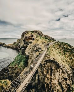 people walking across a rope bridge over the ocean on top of a mountain next to water