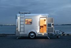 a silver trailer parked next to the ocean at night with its door open and lights on