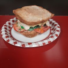 a sandwich sitting on top of a white and red checkered plate next to a cup