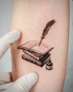 a person with a tattoo on their arm holding a book and a feather quill