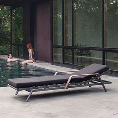 a woman sitting in the water next to a pool with a chaise lounge chair