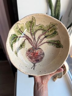 a hand holding a bowl with a plant painted on it