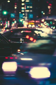 many cars are driving down the busy street at night time, with city lights in the background