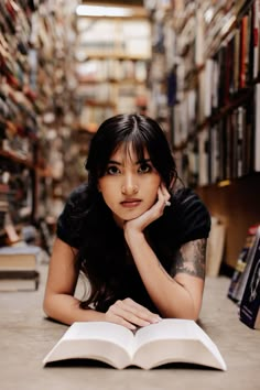 a woman laying on the floor with an open book in front of her and looking at the camera