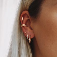 a woman with blonde hair wearing two gold ear cuffs and a pair of diamond hoop earrings