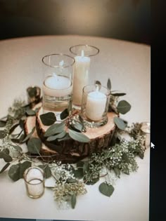 candles and greenery are arranged on a wood slice for a centerpiece or table decoration