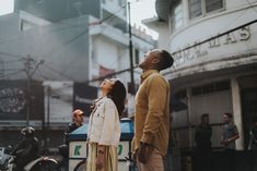 a man and woman standing in the street looking up into the sky with their eyes closed