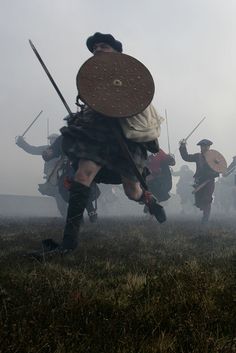 men dressed in medieval costumes running through the grass with swords and shields on their heads