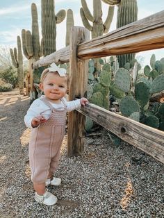 a baby girl standing in front of a cactus