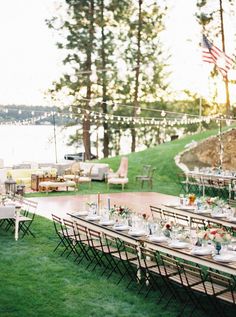 a long table set up with place settings for an outdoor dinner party on the lawn