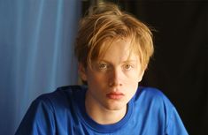 a close up of a person wearing a blue shirt and looking at the camera with a serious look on his face