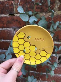 a hand holding up a yellow plate with bees on it and the word sara painted on it