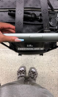 a person is holding an electronic device in their hand while standing next to a suitcase