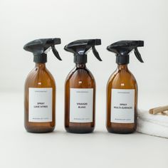 three brown bottles with black sprayers on them sitting next to a white towel and some scissors