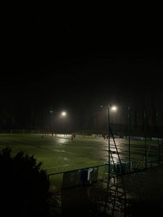 a soccer field at night with lights on and people playing in the rain behind it