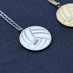 two volleyball necklaces sitting on top of a blue cloth covered table next to each other