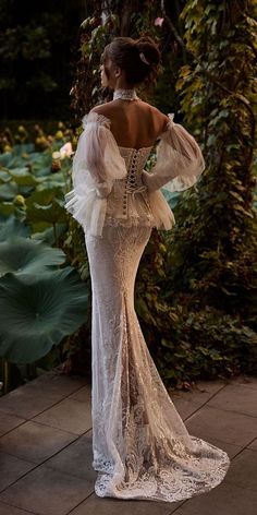 the back of a woman in a white dress standing on a brick walkway surrounded by greenery