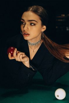 a woman holding an apple while sitting next to a pool table with two balls on it