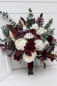 a bridal bouquet with red and white flowers, greenery and leaves on the side of a building